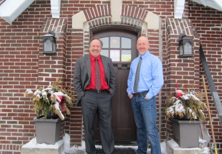 PRI Group founders standing in front of a brick building entrance with winter planters